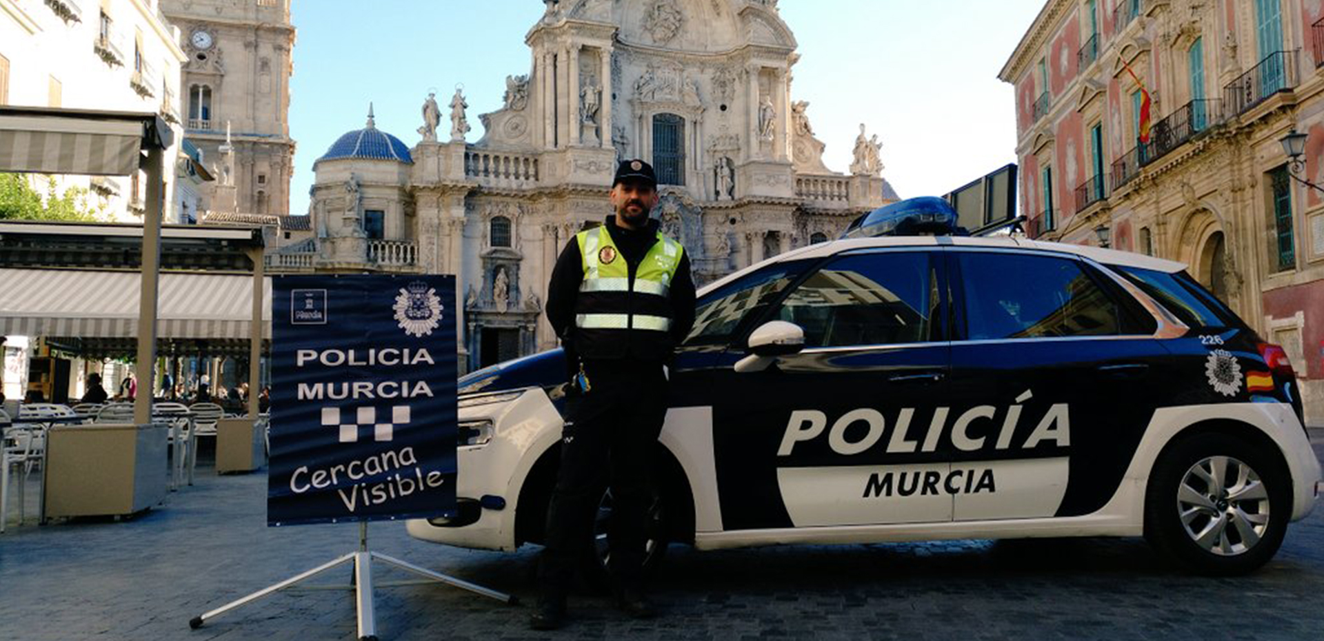 Agente de policía con el cartel de la campaña de Policía Visible en la Plaza del Cardenal Belluga